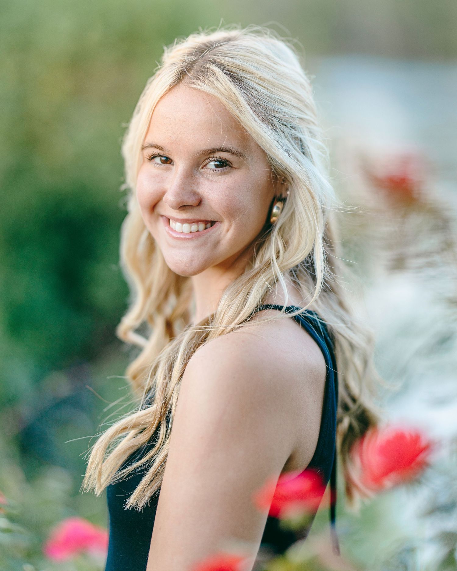 Portrait session in a garden setting with soft natural lighting and red flowers in the background.