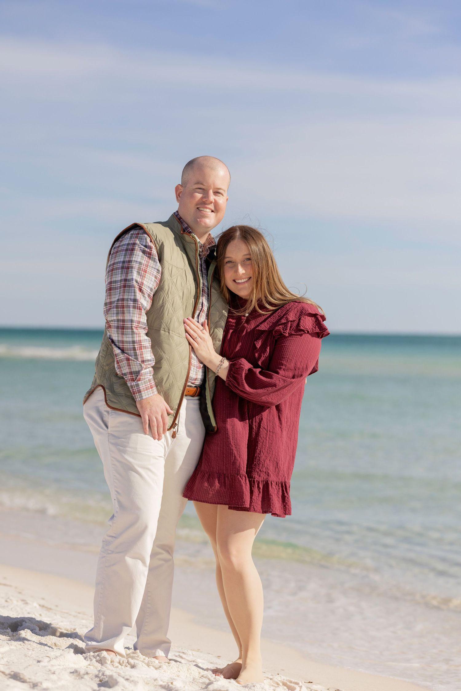 Couple standing together smiling on a white sand beach with turquoise ocean water in the background.