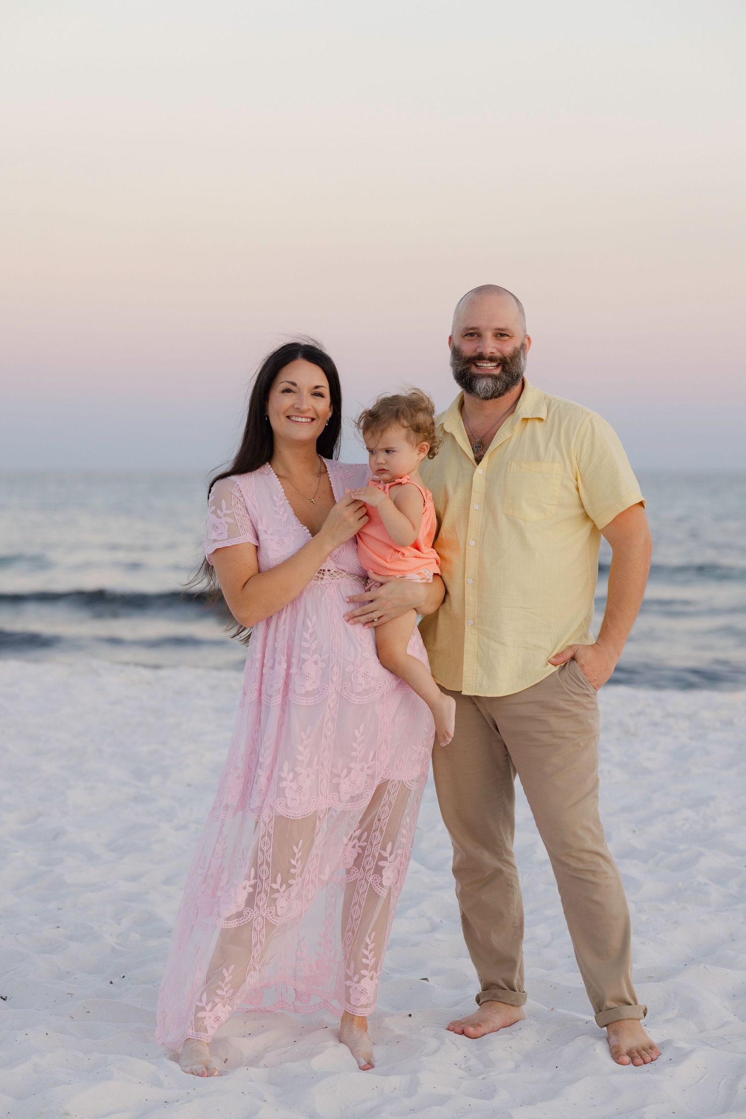 A family stands together on a beach at dusk with waves rolling in behind them.