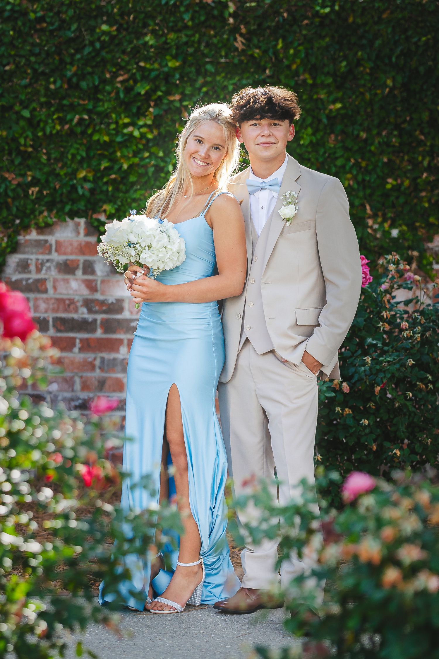 Wedding couple poses in romantic garden setting with light blue bridesmaid dress and tan suit details.