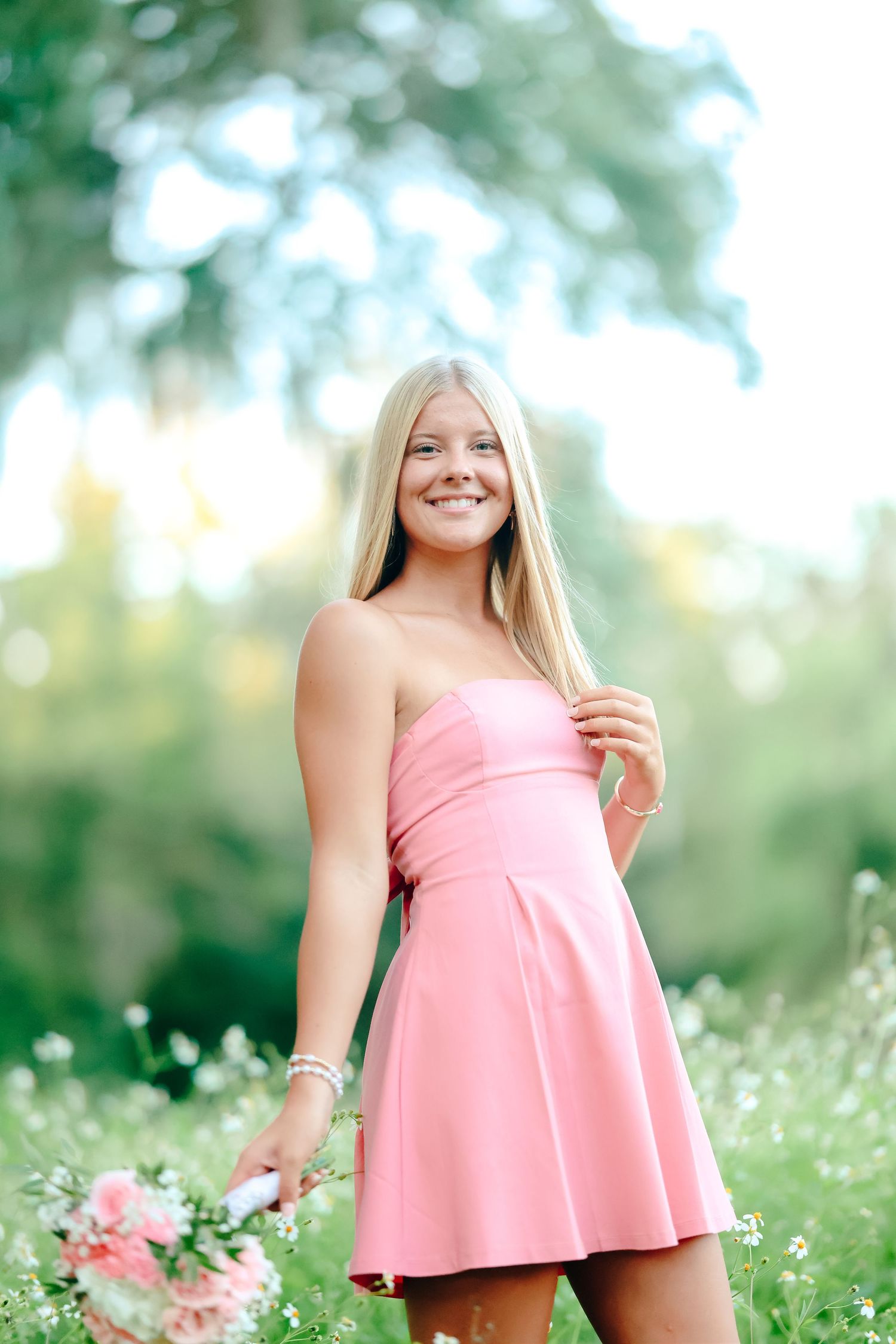 A strapless pink summer dress styled with a flowy skirt in a sunny meadow filled with white flowers.