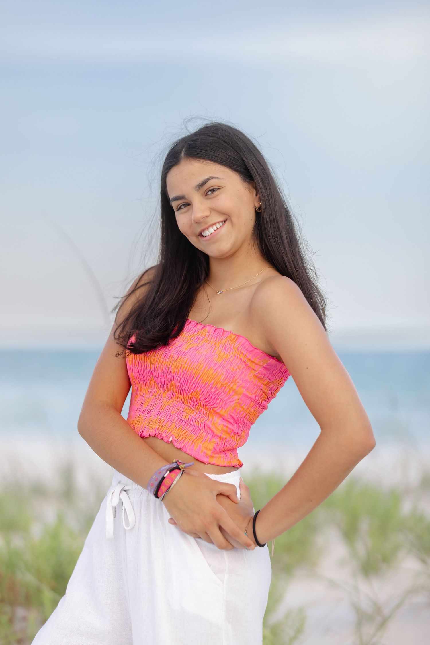 Woman in neon coral crop top smiles joyfully during beach photoshoot.