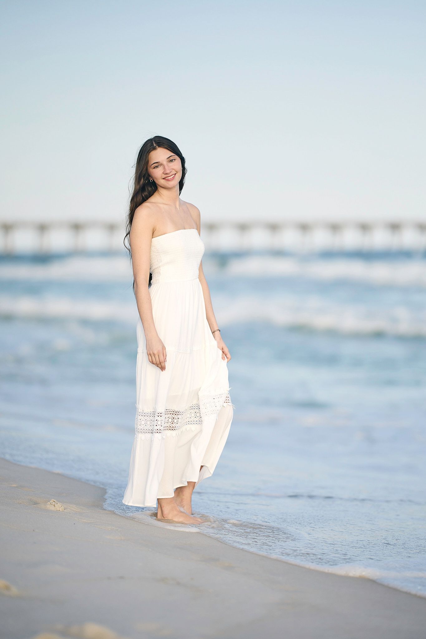 Casual beach portraits with white sundress against gentle ocean waves.