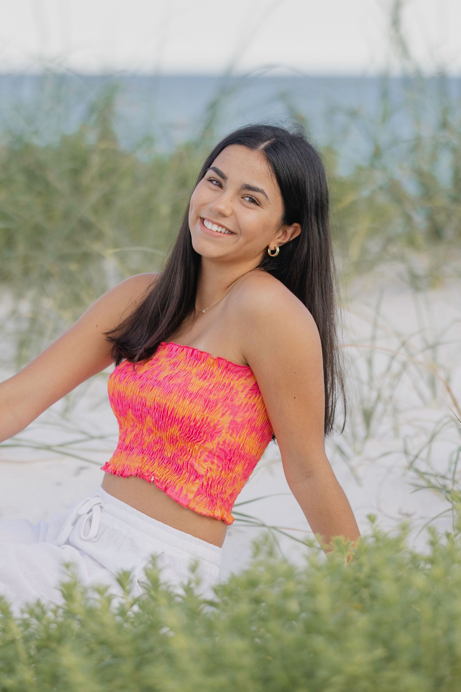 A series of beach portraits showing someone in a bright coral patterned top posing in beach grass at sunset.