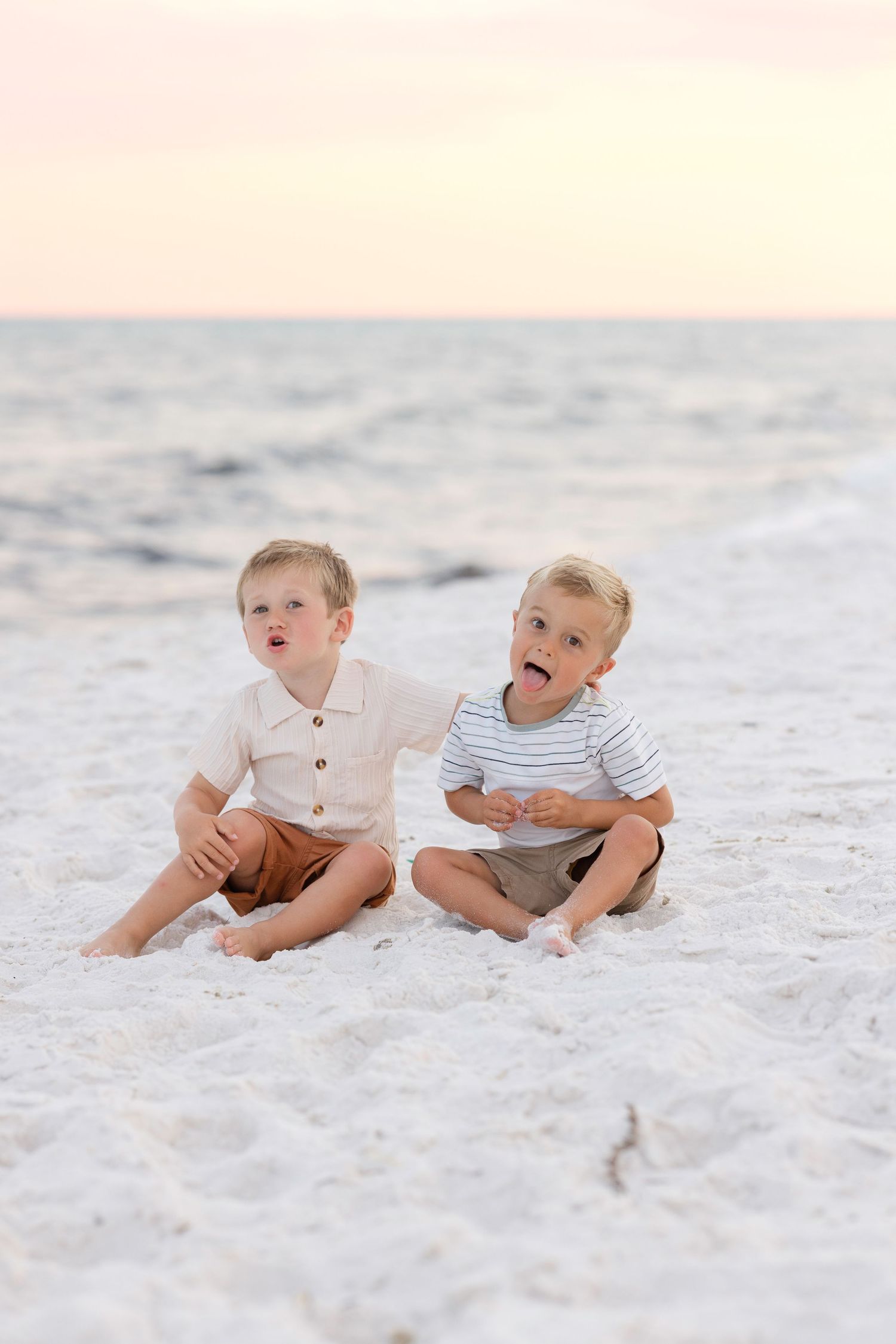 Young children sit together playing in pristine white sand at the beach.
