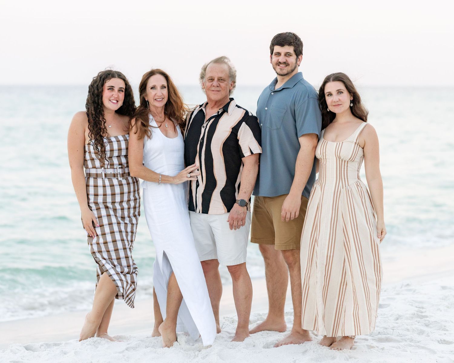 Family of five poses together smiling at beach shoreline during golden hour sunset photography session.