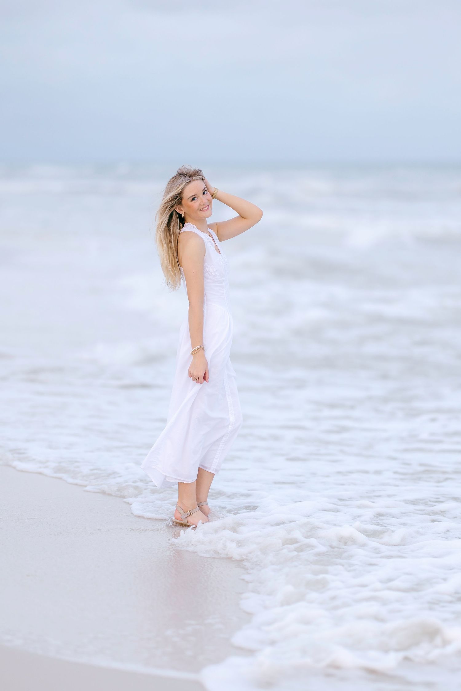 Person in white dress enjoying ocean breeze at water's edge.