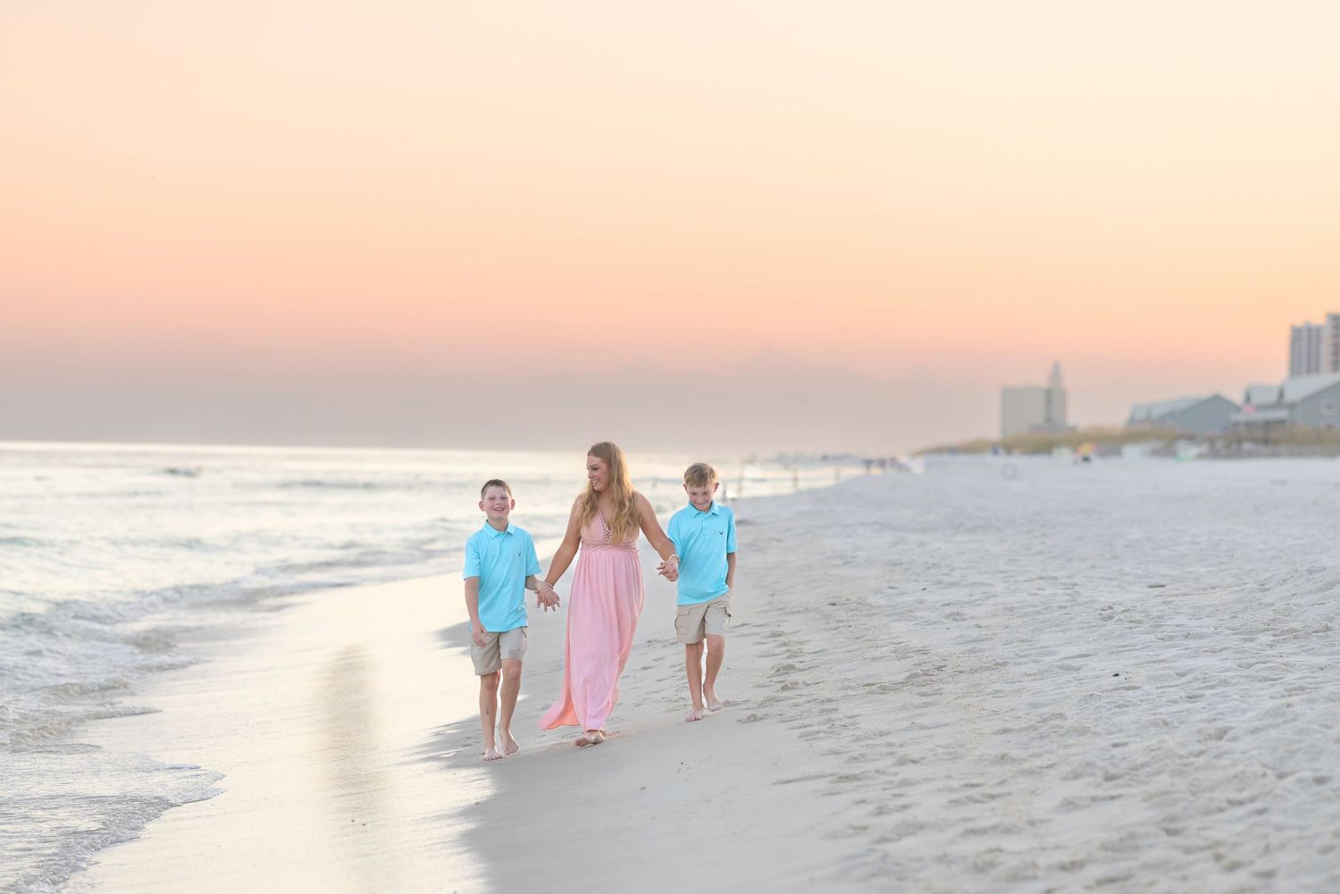 Beach goers walk along the shoreline at sunset while waves gently roll in on a serene evening.