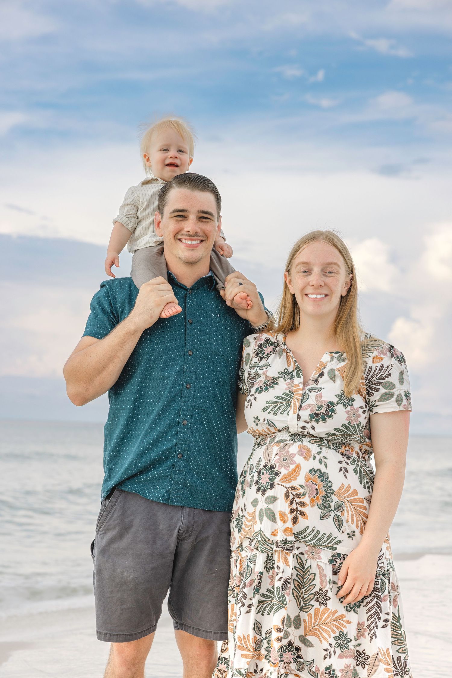Happy family takes candid photos together on beach with waves and cloudy sky in background.
