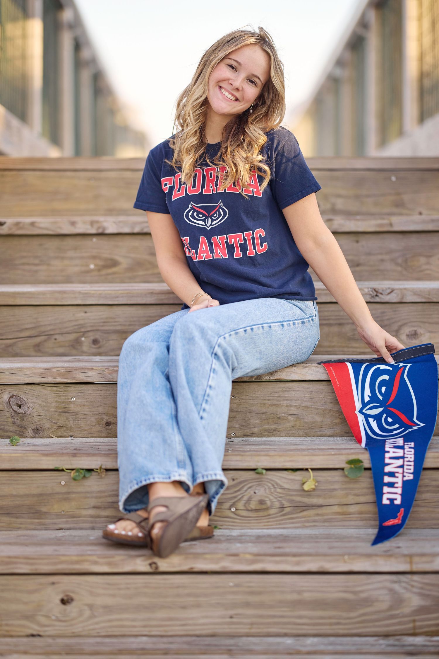 Someone wearing a Florida Gators t-shirt and jeans sits casually on wooden steps with a team pennant flag.