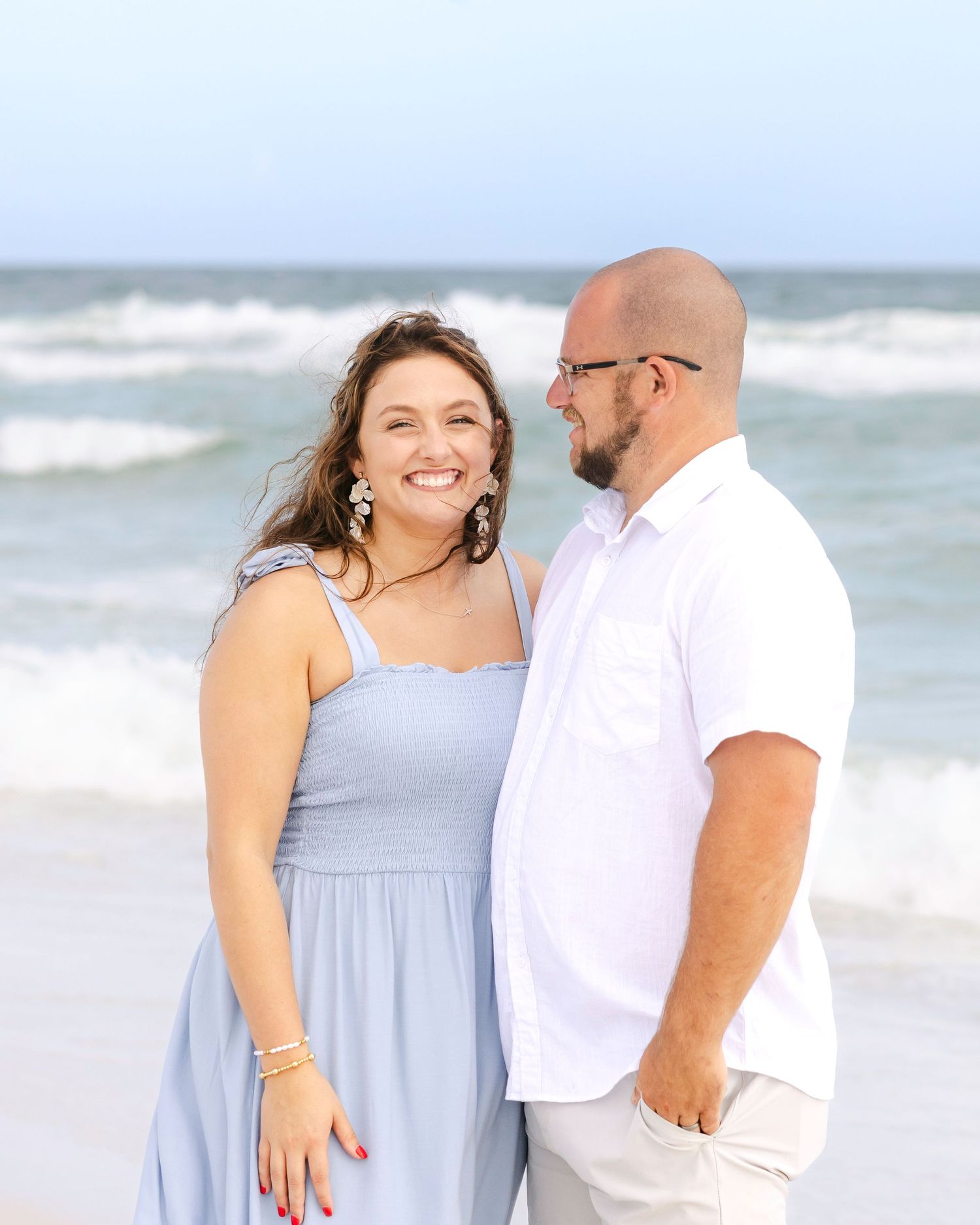 Couple in coordinated blue and white outfits shares joyful moment on sunny beach.