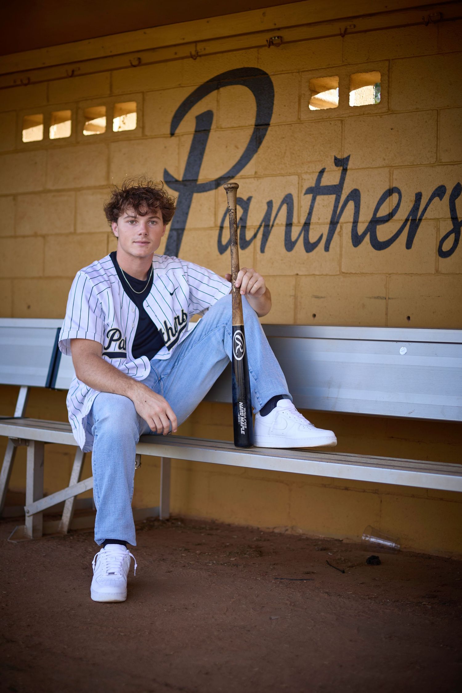 Baseball player sits in dugout wearing pinstriped uniform during game.
