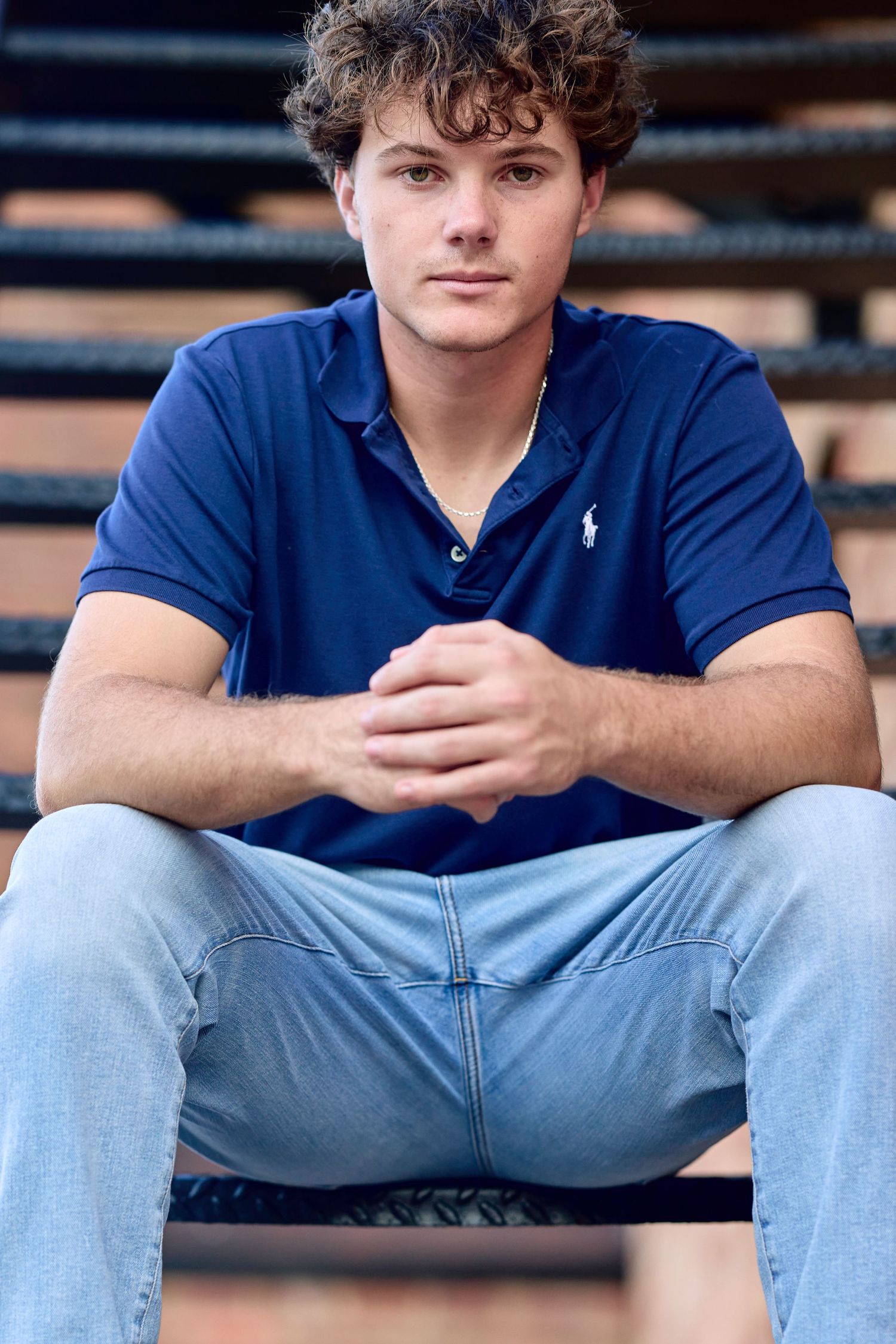 A person in a navy blue Ralph Lauren polo shirt and light jeans sits on wooden bleachers.