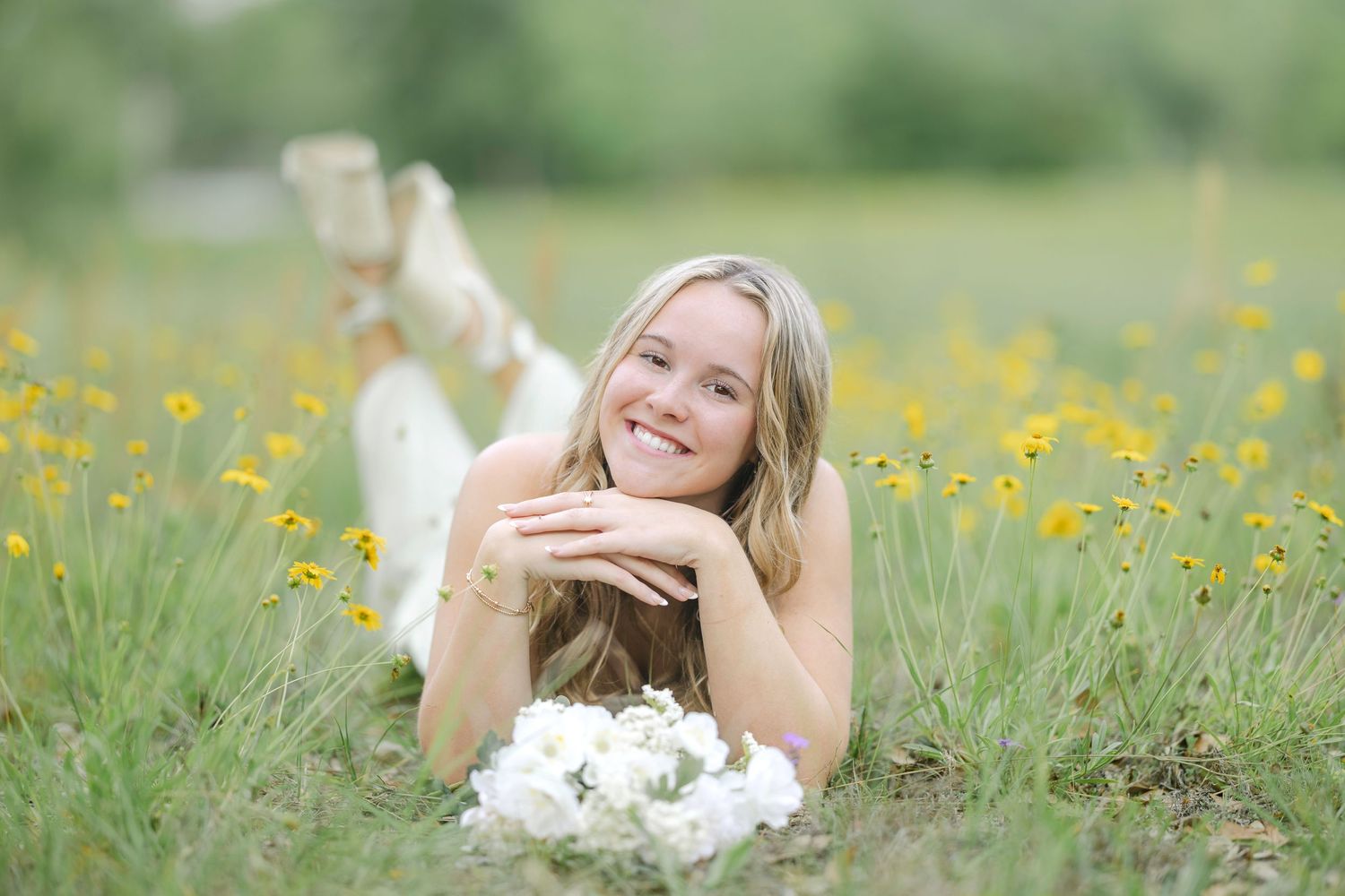 Woman relaxing in a grassy field surrounded by blooming yellow flowers and natural scenery.