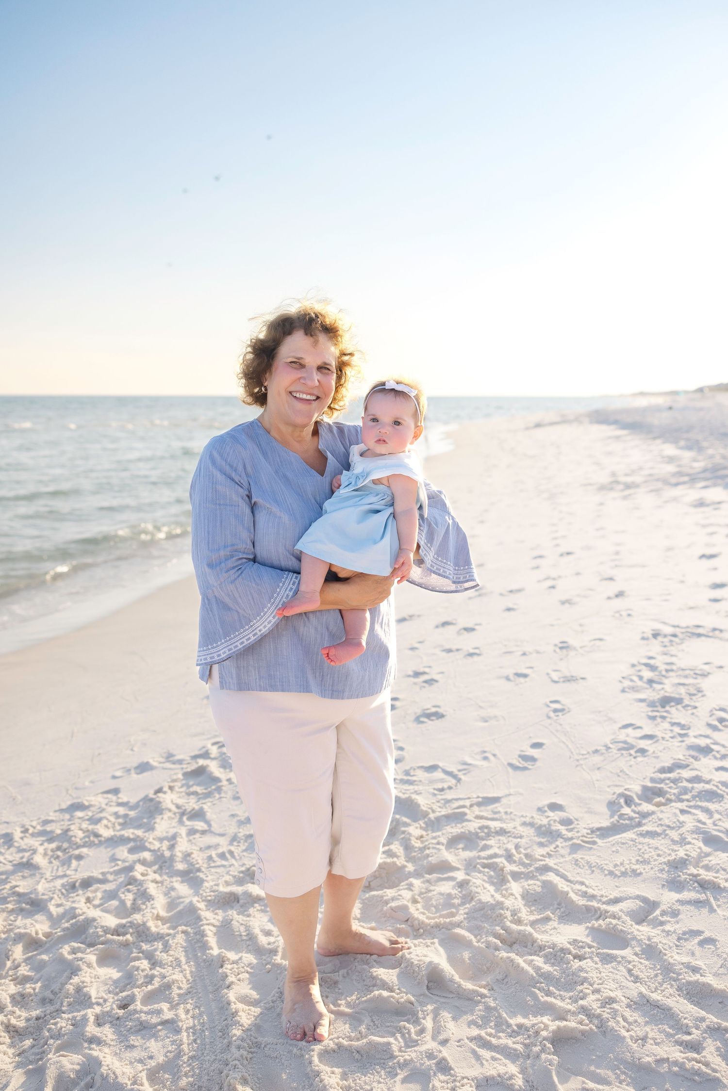 Multiple connected images of a beach scene with a woman in blue holding a baby against a bright sandy backdrop.