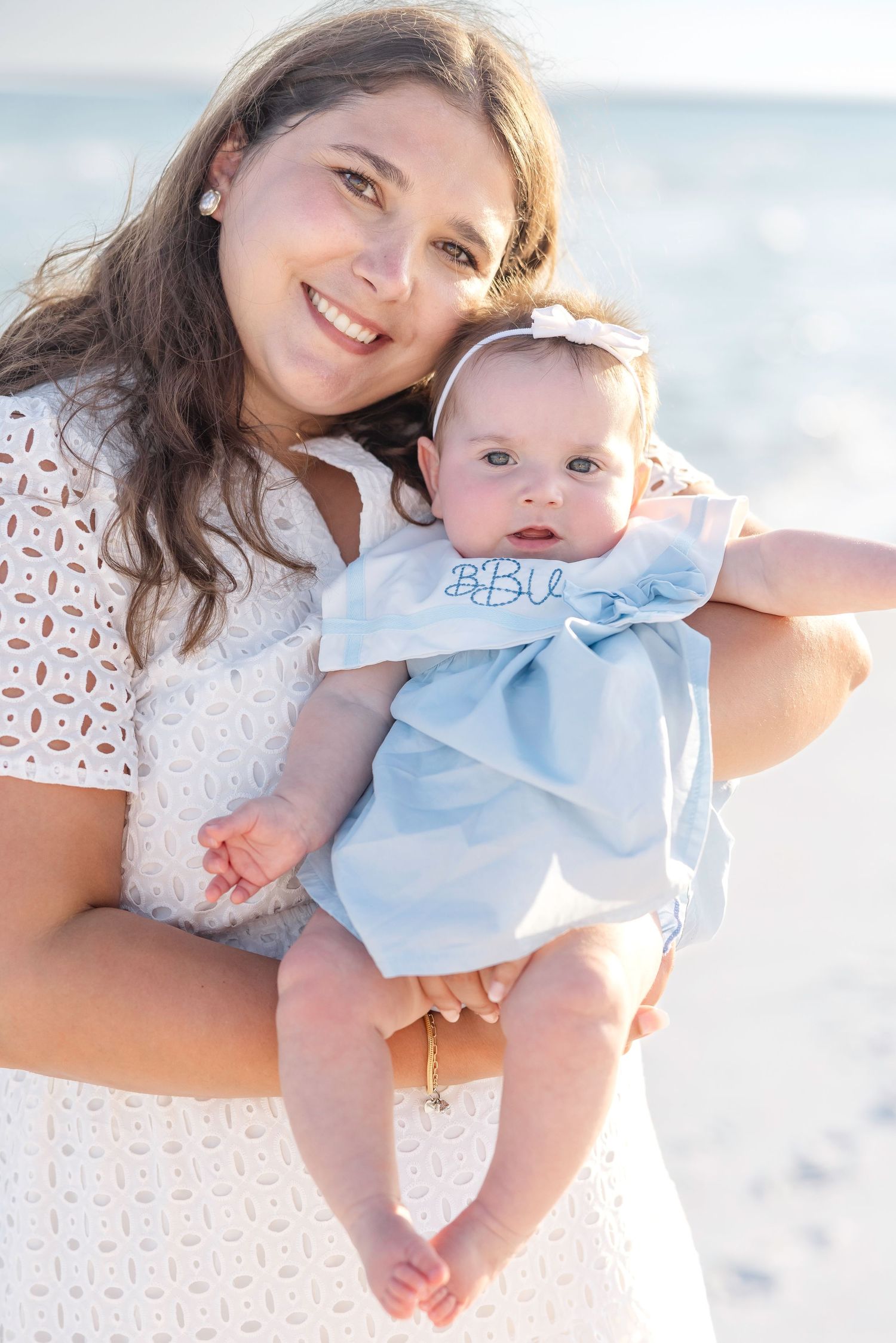 Four connected beach photos showing tender moments between a woman in white lace and baby in light blue on the sand.