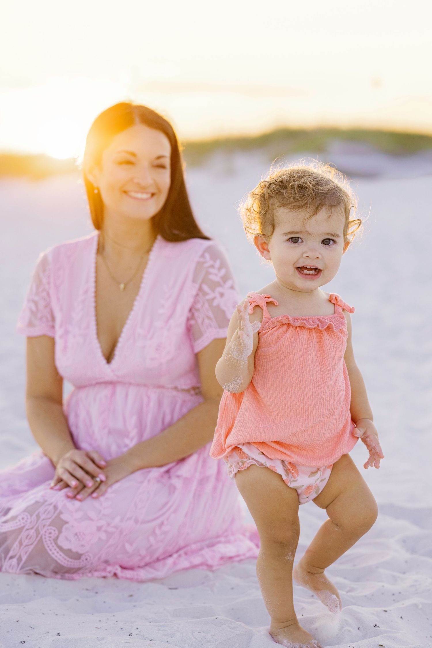 A tender beach moment captured during golden hour with soft pink and coral tones.
