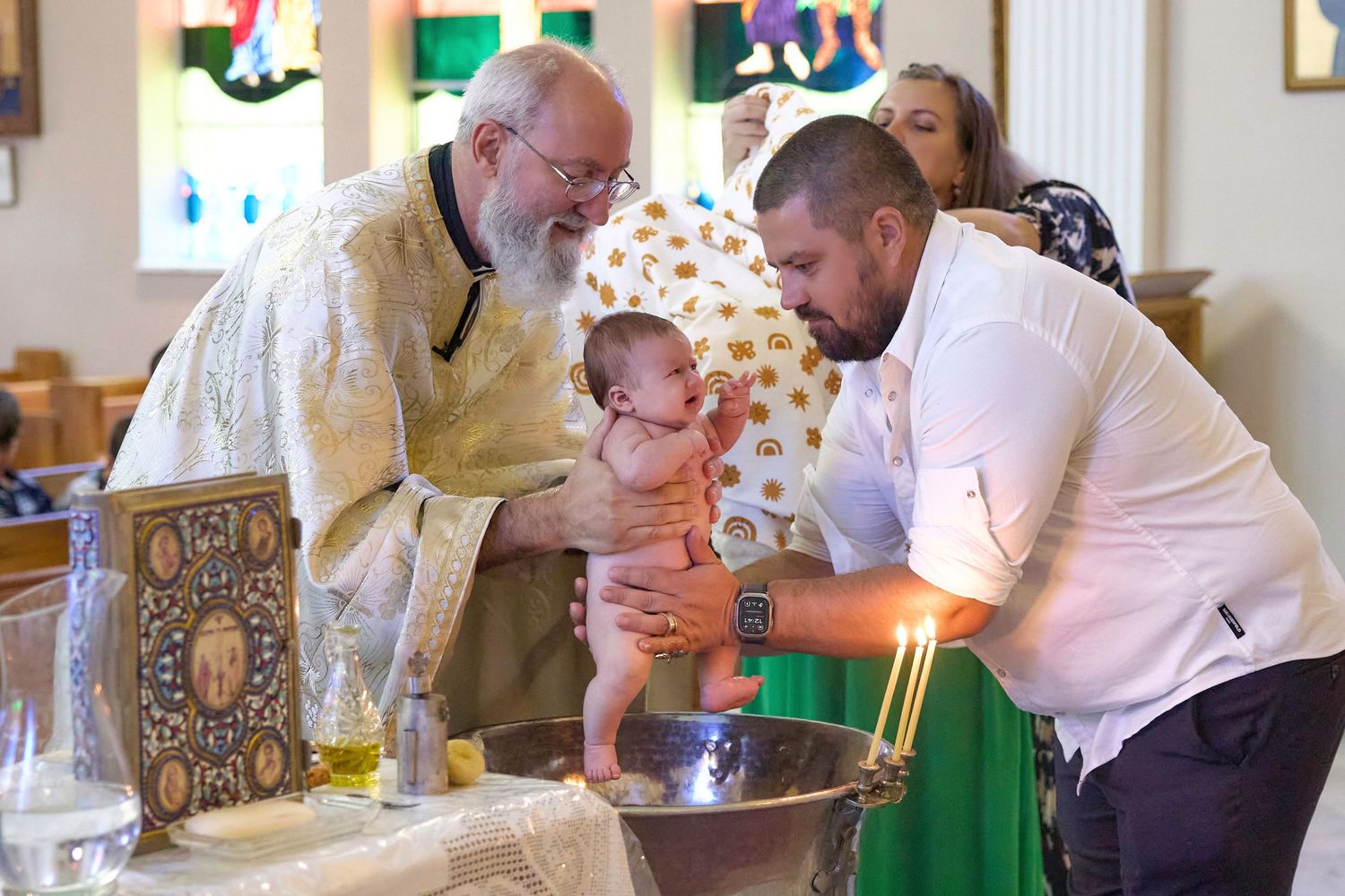 A baby is being baptized in a church ceremony with clergy and family members participating in the sacred ritual.