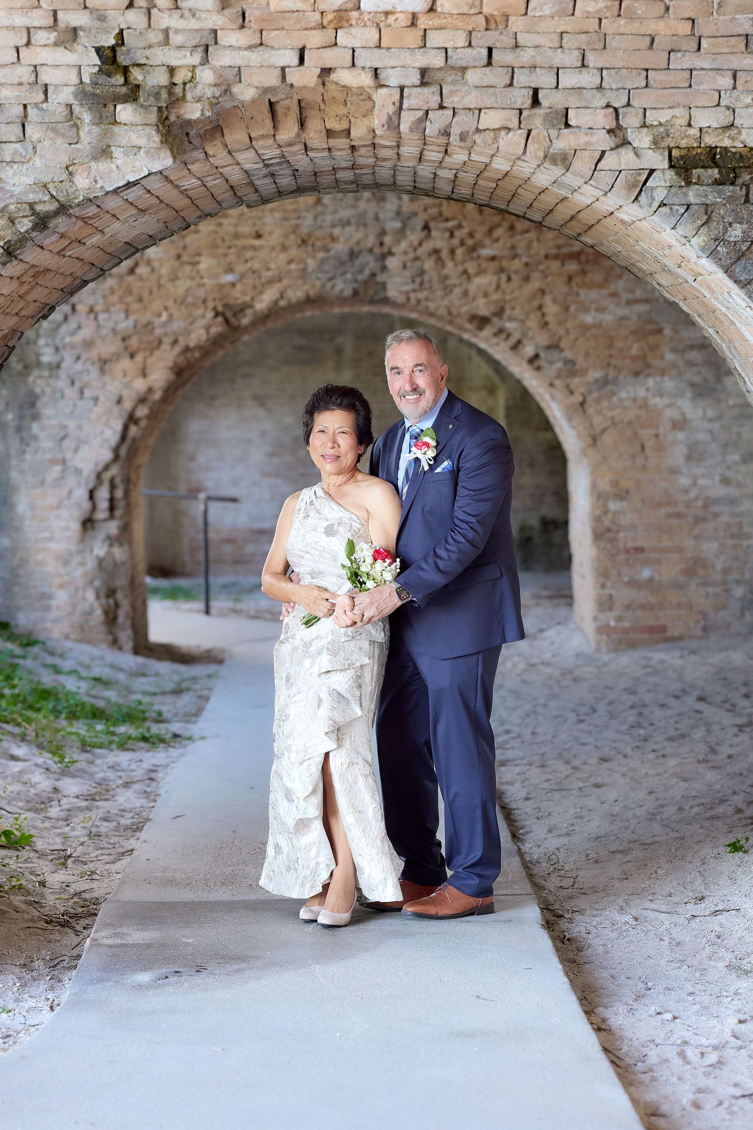 A couple poses together under a series of brick archways at a historic location for their wedding photos.