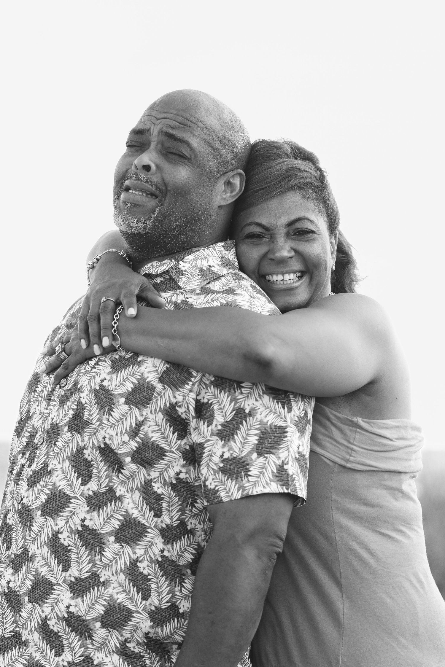 A bald man and smiling woman share a warm embrace in a black and white portrait photo.