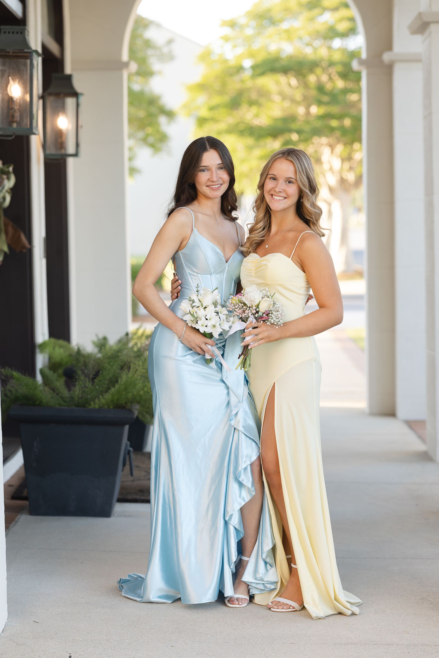Formal portrait of two people in elegant evening gowns under a columned archway.