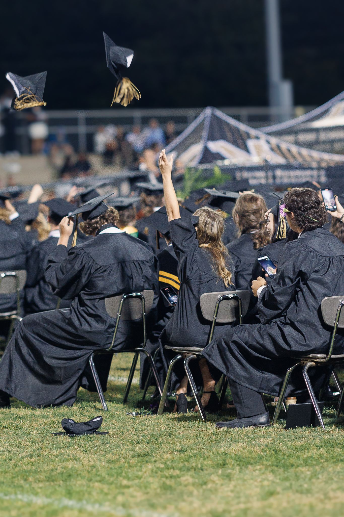 Graduates throw their caps in the air while seated in folding chairs during commencement ceremony.
