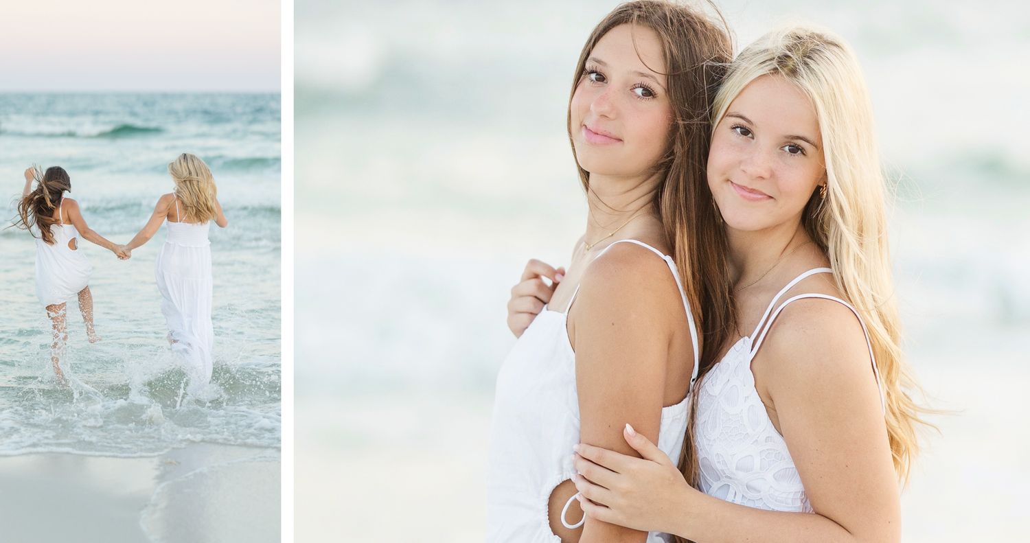 Two people in white dresses embrace while standing on a sandy beach with ocean waves in the background.