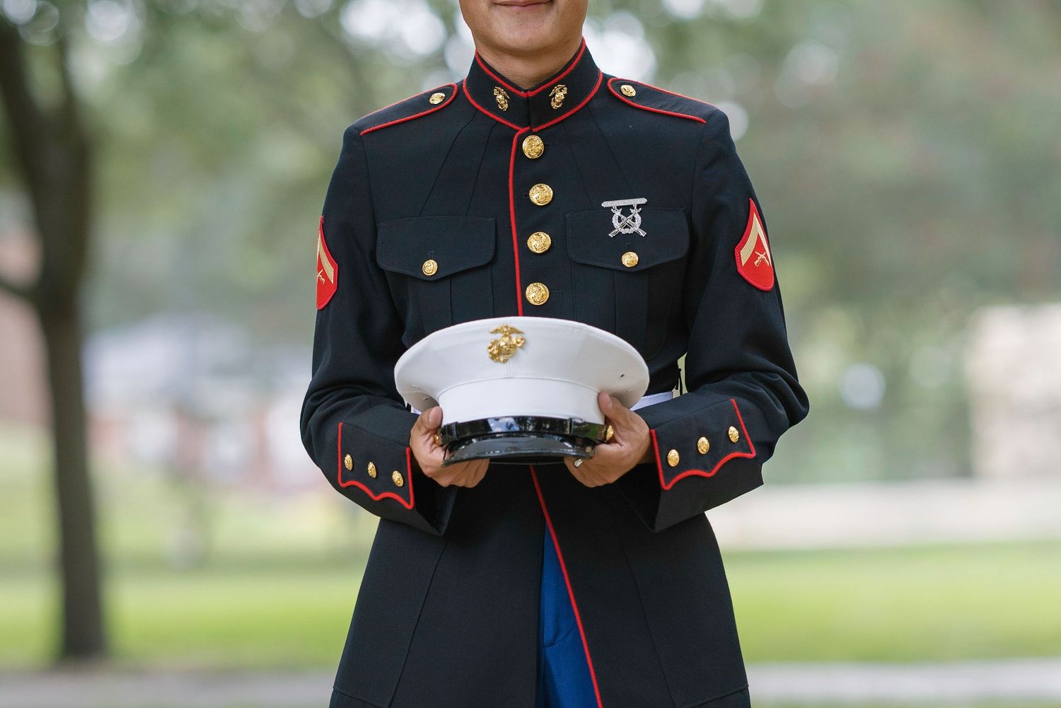 Marine in dress blues uniform holding white cover cap outdoors.