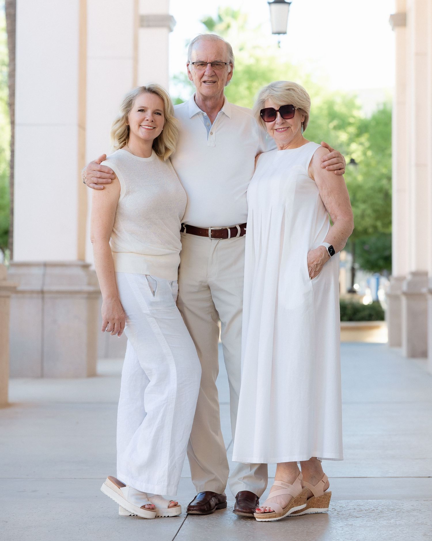 Three family members smiling together in coordinating white and beige outfits.