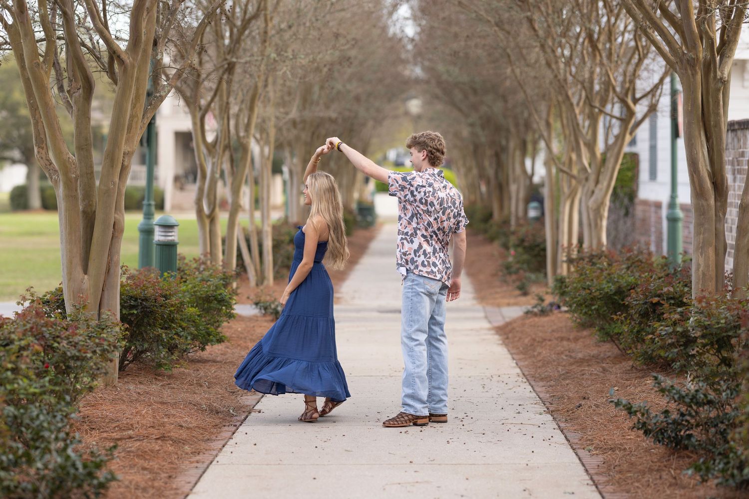 A couple dances together on a tree-lined pathway during a romantic outdoor photo session.