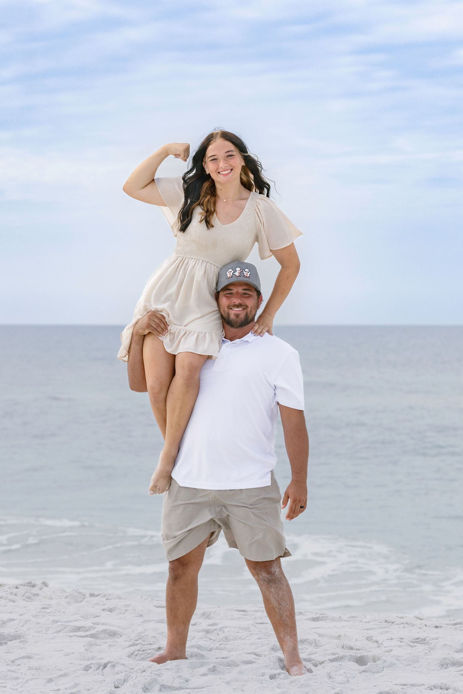 Smiling man carrying laughing young woman on his shoulders on a sunny beach.
