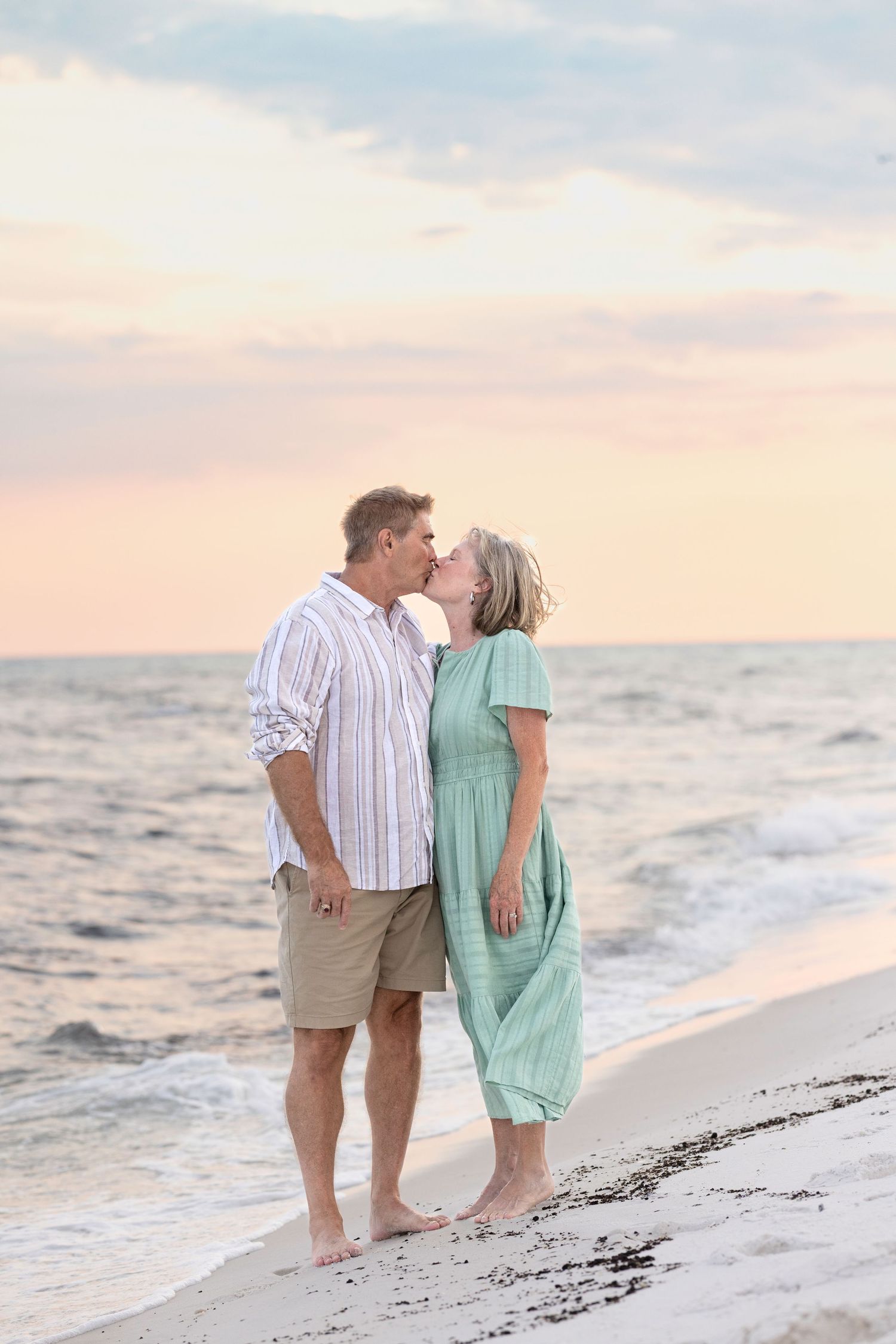 A couple shares a romantic moment while walking along a sunset beach in light summer attire.