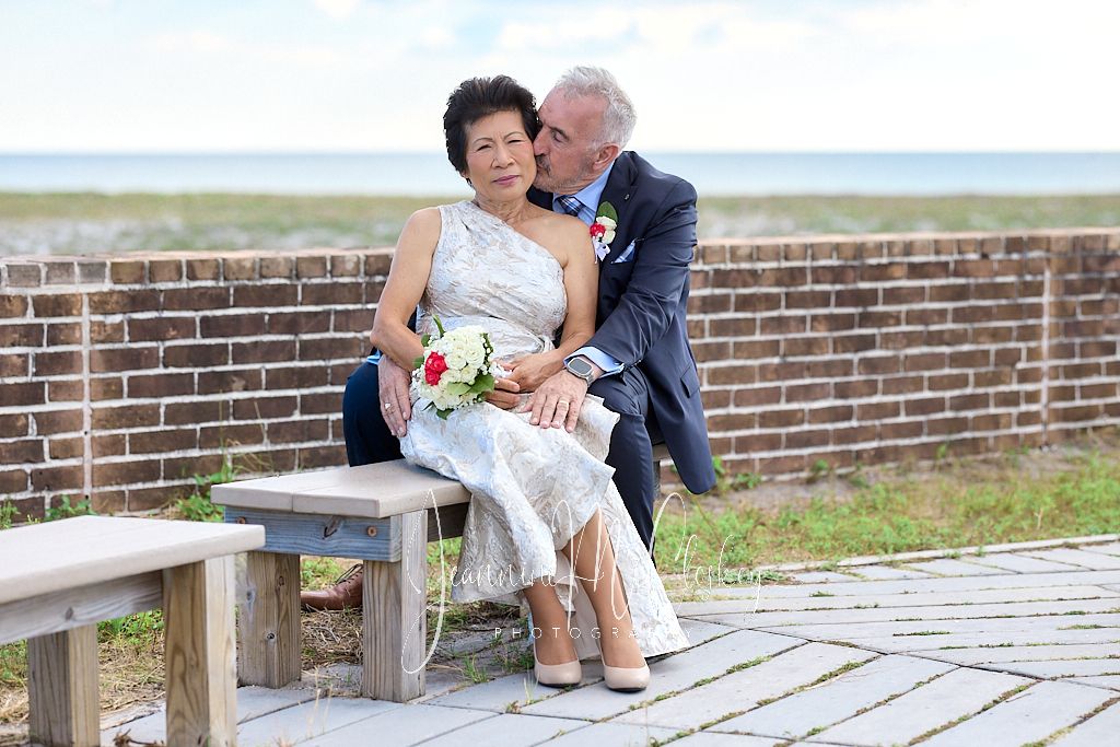 A couple sits together on wooden benches by a brick wall overlooking a scenic waterfront view.