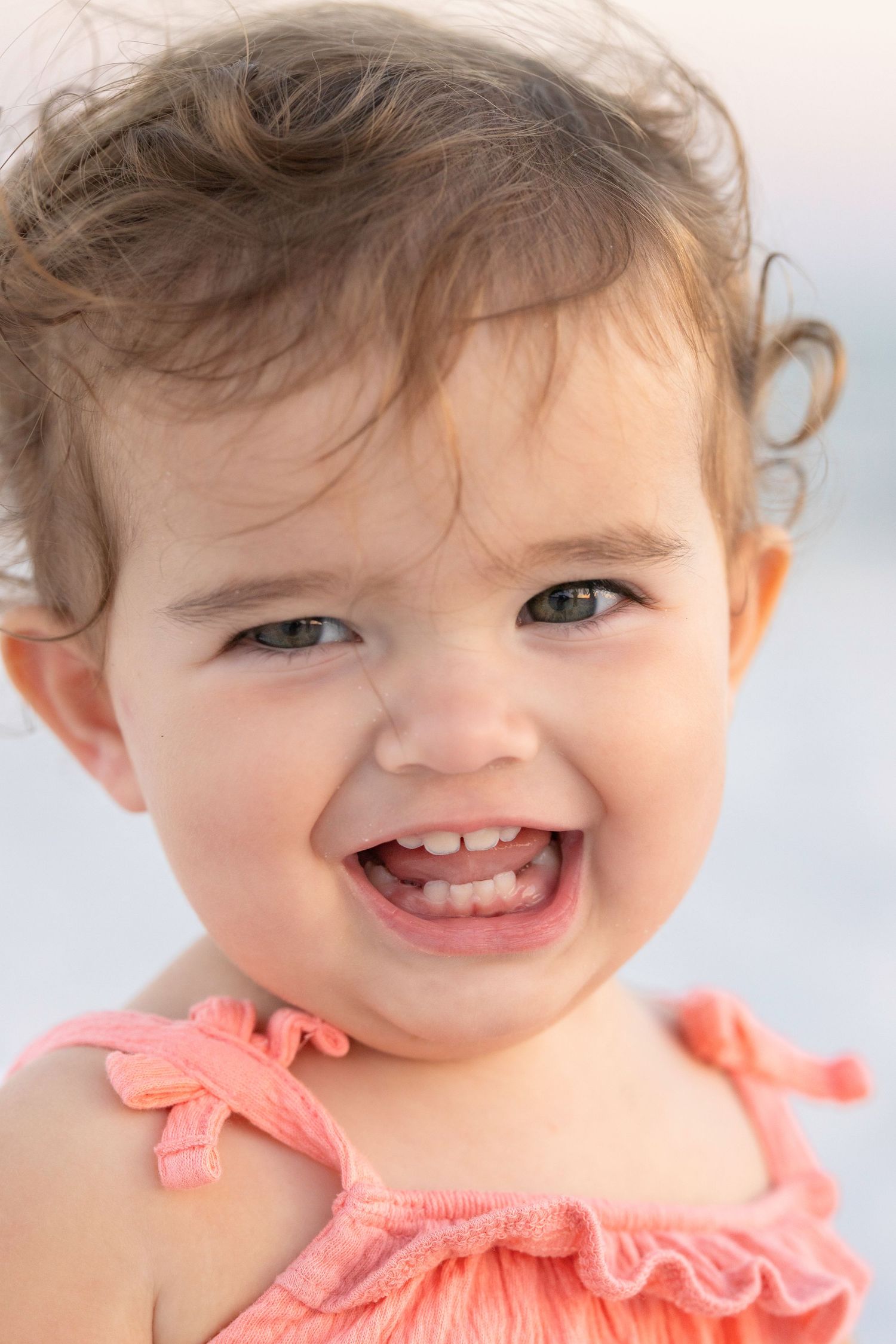 Close-up portraits capture sweet expressions with coral pink ruffled details against a soft, bright background.