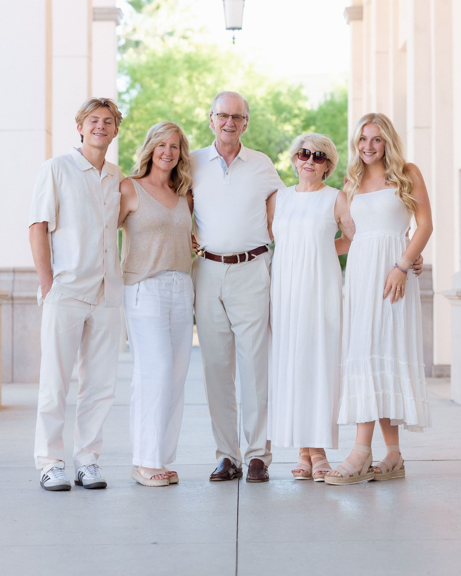 Five family members smile together in white and neutral outfits during an outdoor portrait session.
