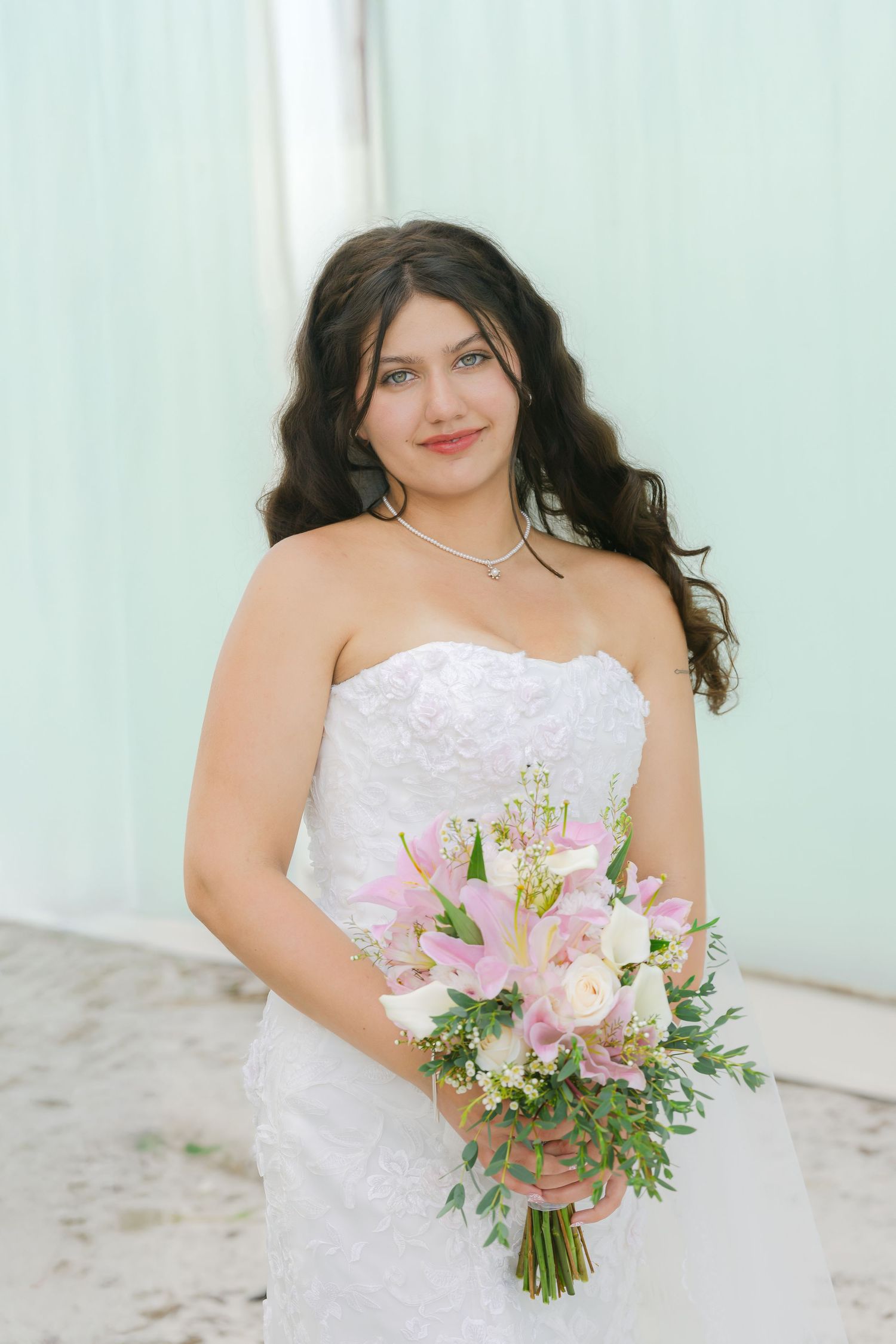 Bride holding a pink and white floral bouquet poses against a mint green wall.