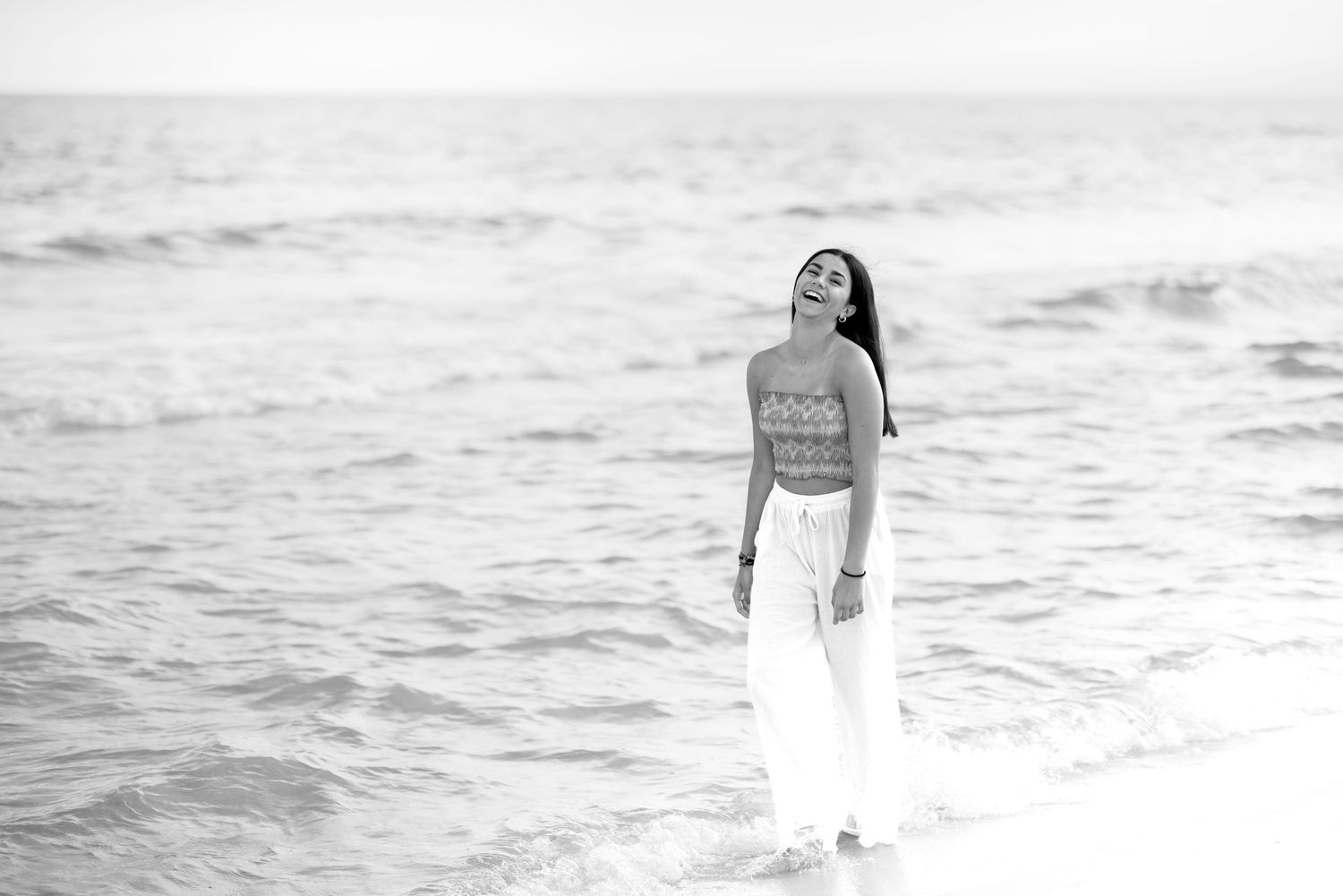 Black and white beach portrait with flowing white pants and casual top by the waves.