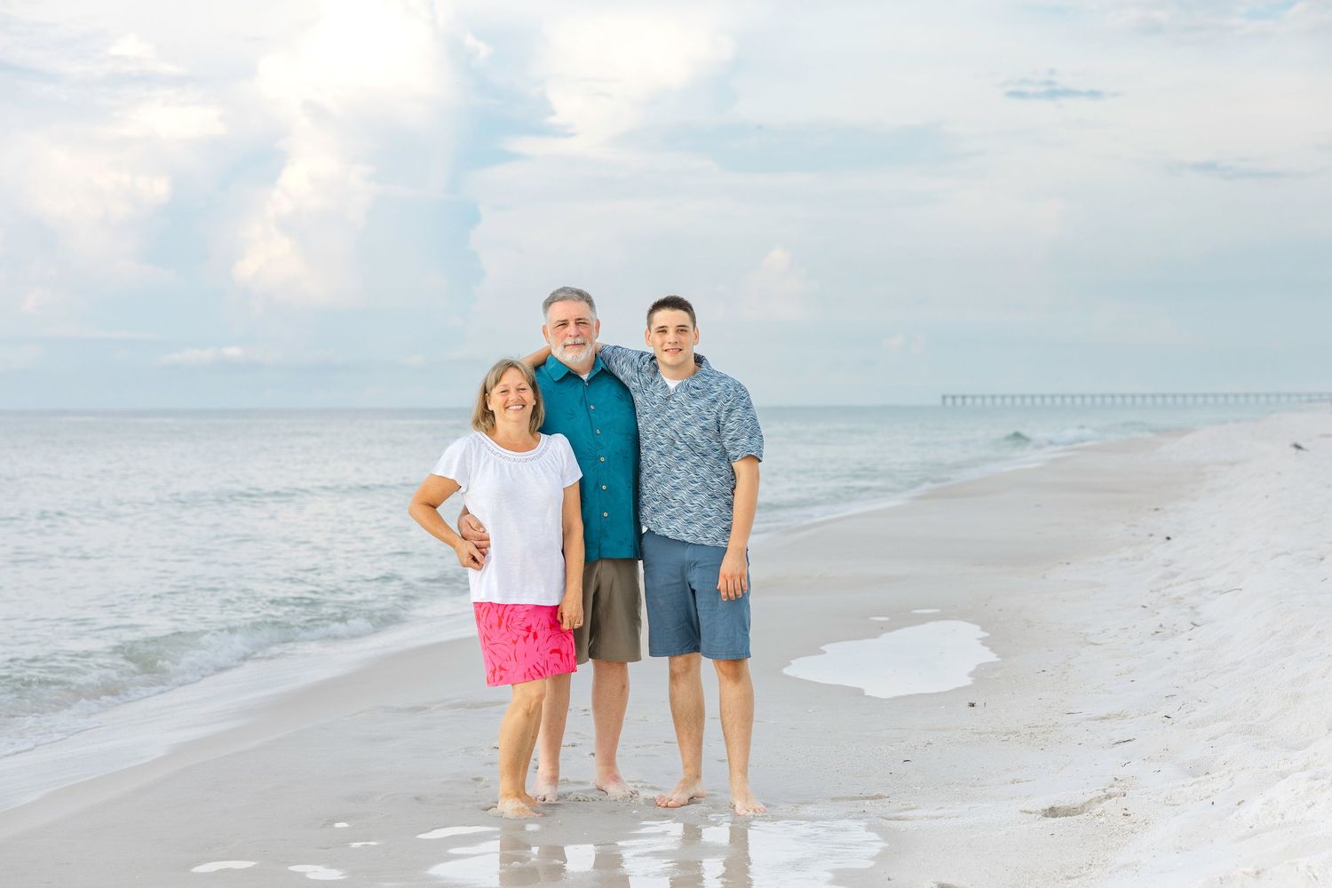 Beach portrait session of people walking and posing along a sunny shoreline with waves and white sand.