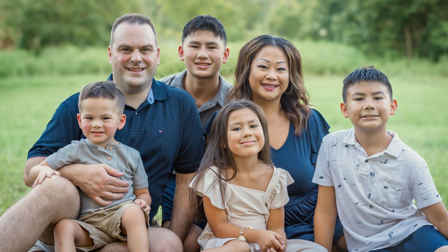 Extended family poses together outdoors in coordinated outfits for professional portrait session in park setting.
