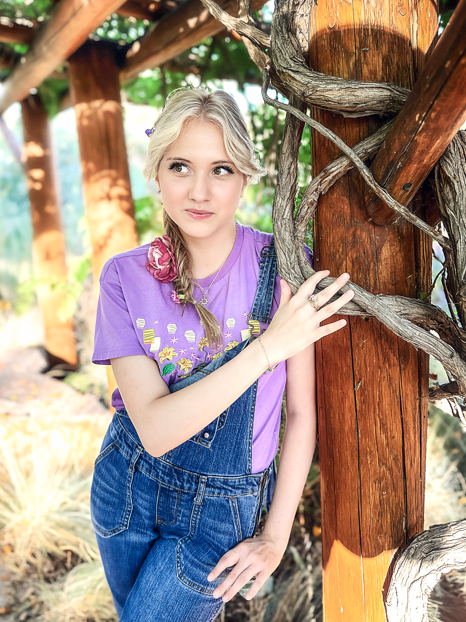 Person in denim overalls and purple top posing playfully against rustic wooden posts.