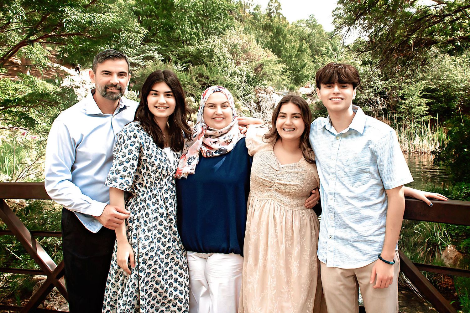 A group poses together in coordinated outfits near a rustic wooden fence in a garden setting.