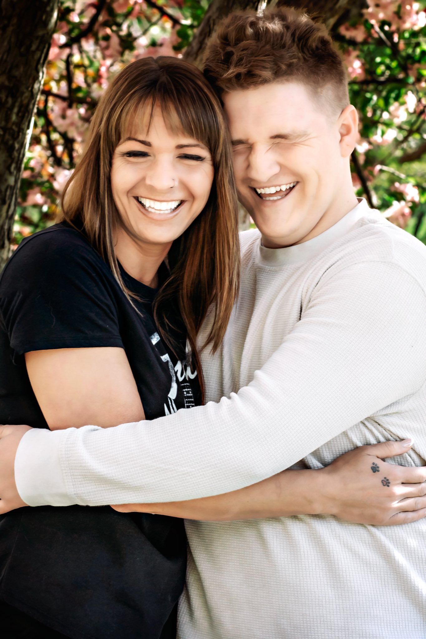Candid outdoor portrait of couple embracing under flowering tree branches.