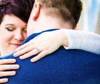 Close-up of an intimate embrace showing hands with a wedding ring against a blue sweater.