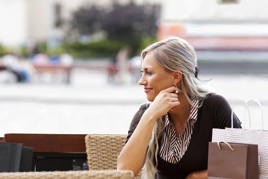 Woman in black top relaxing at outdoor cafe with urban setting in background.