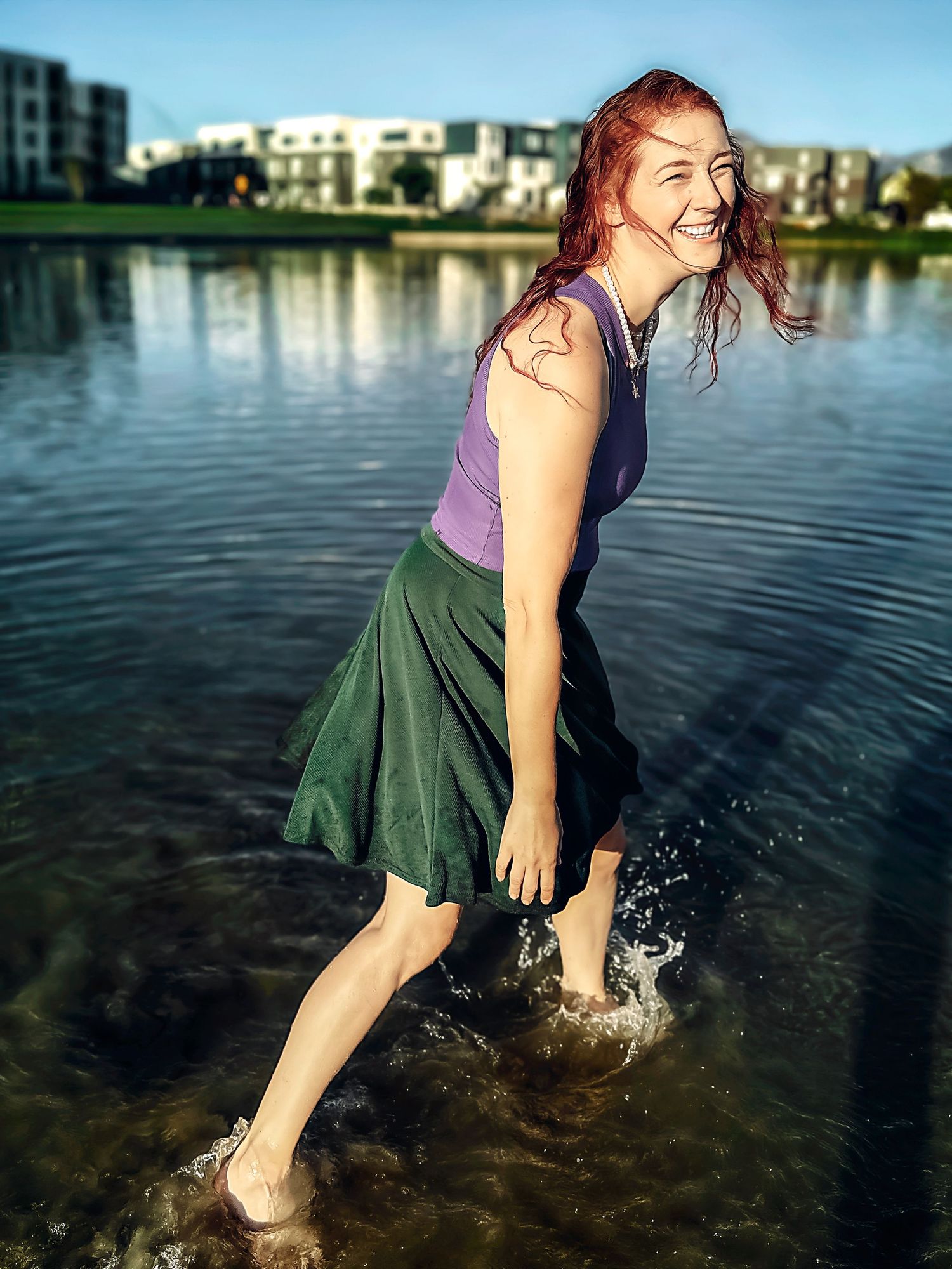 Someone splashing and playing in the lake water while wearing a purple top and green skirt.