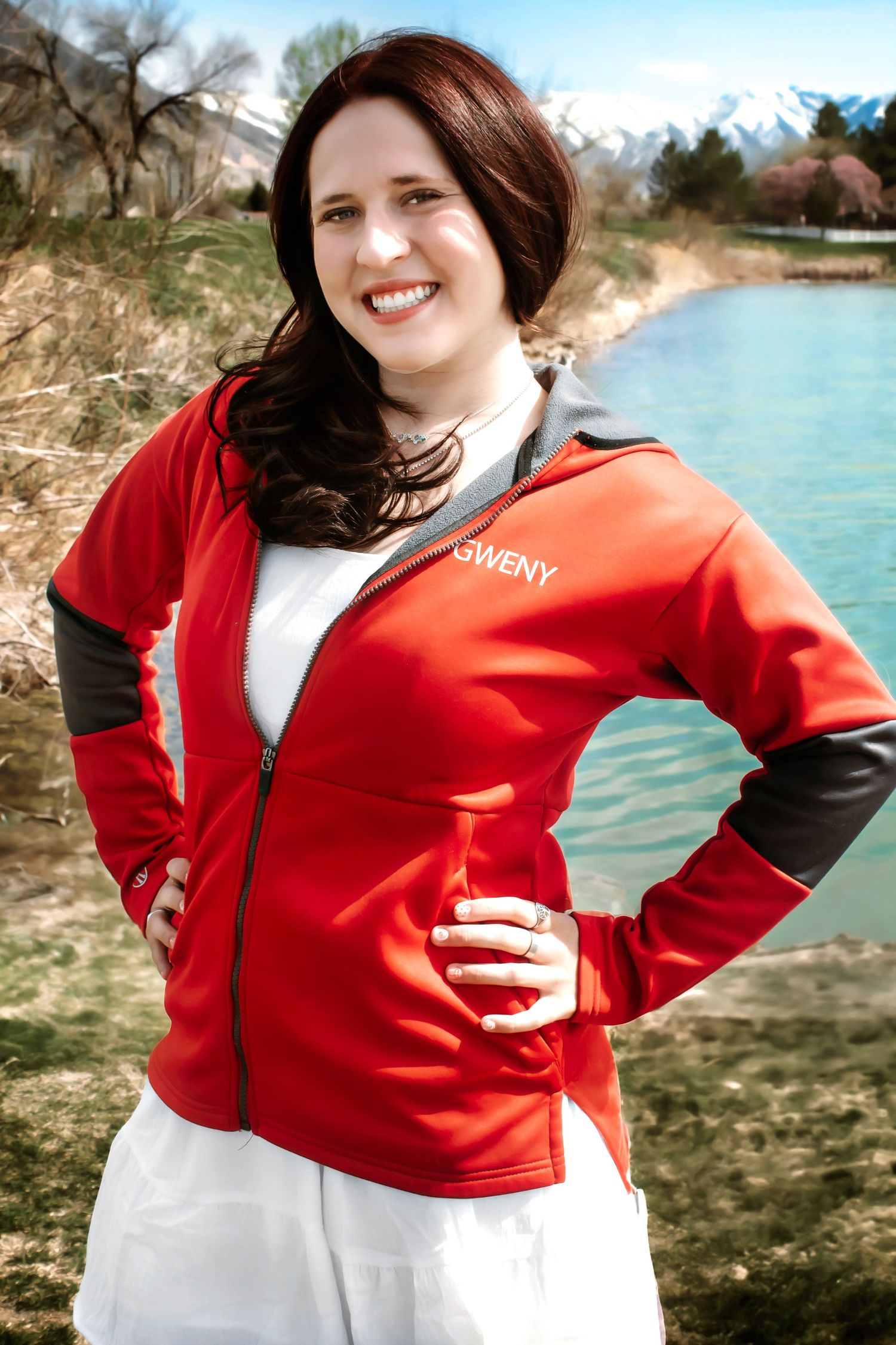Person wearing red athletic jacket poses near mountain lake.