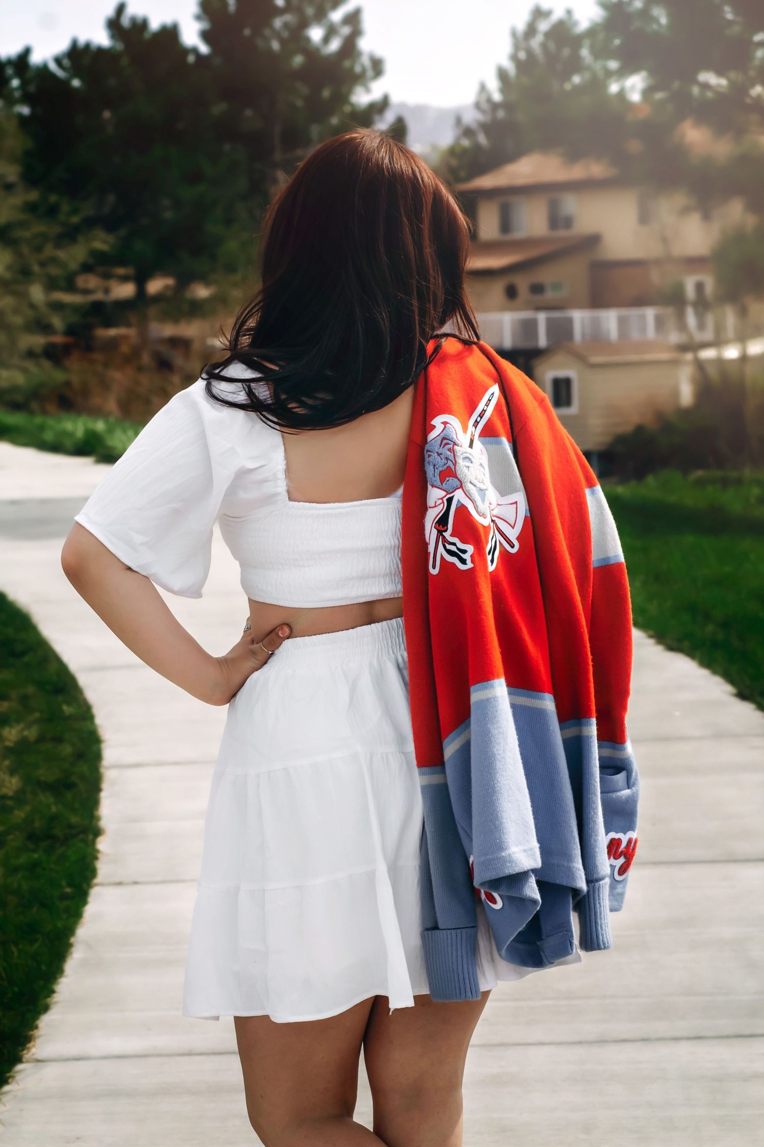 Back view of person in white dress holding red and blue sports jacket.