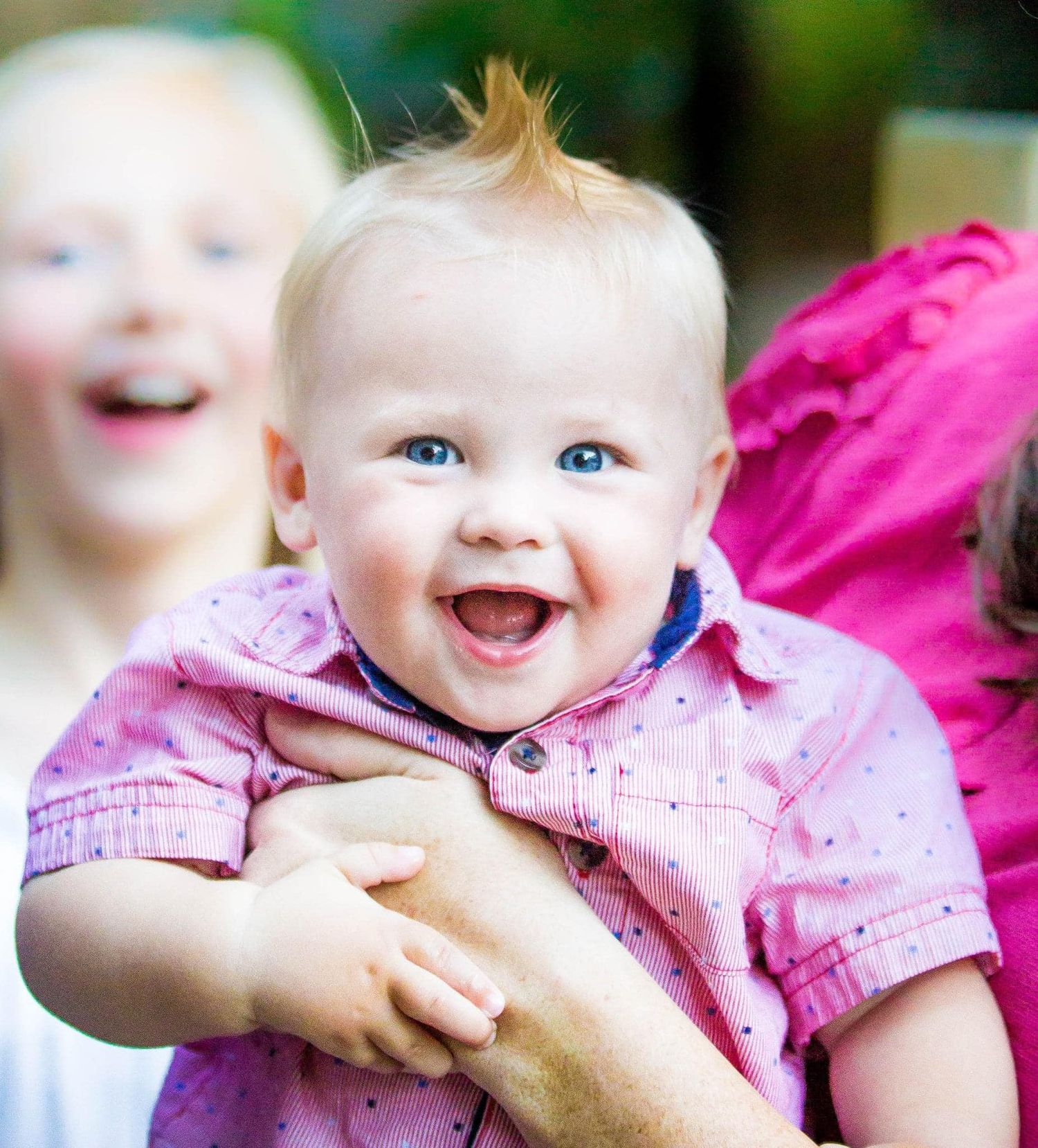 Baby wearing pink outfit smiling and laughing.