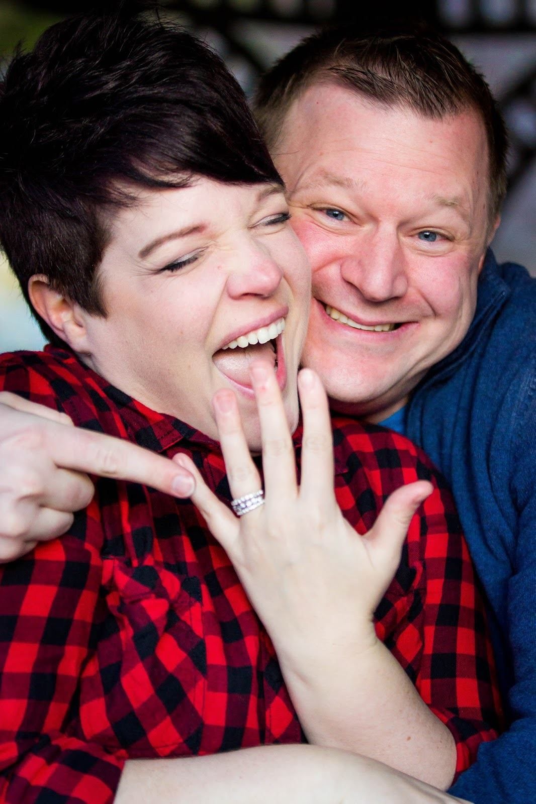 Playful couple in red plaid and blue sharing laughs during photo session.