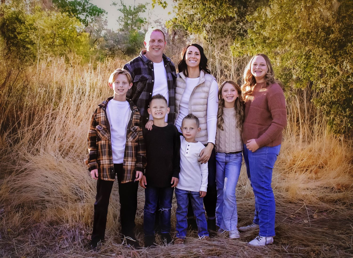 A family group poses together outdoors during autumn against natural foliage.